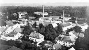 Flugaufnahme aus 1924. Links Erweiterung der Weberei Ost, oberhalb Dach vom „Bader-Haus“ sowie „Böhmische Villa“. Direkt neben dem „Lang-Haus“ das Dach vom „Hummelgütl“ an der Bahnhofstrasse 6. Im Hintergrund die Firma Feurstein.